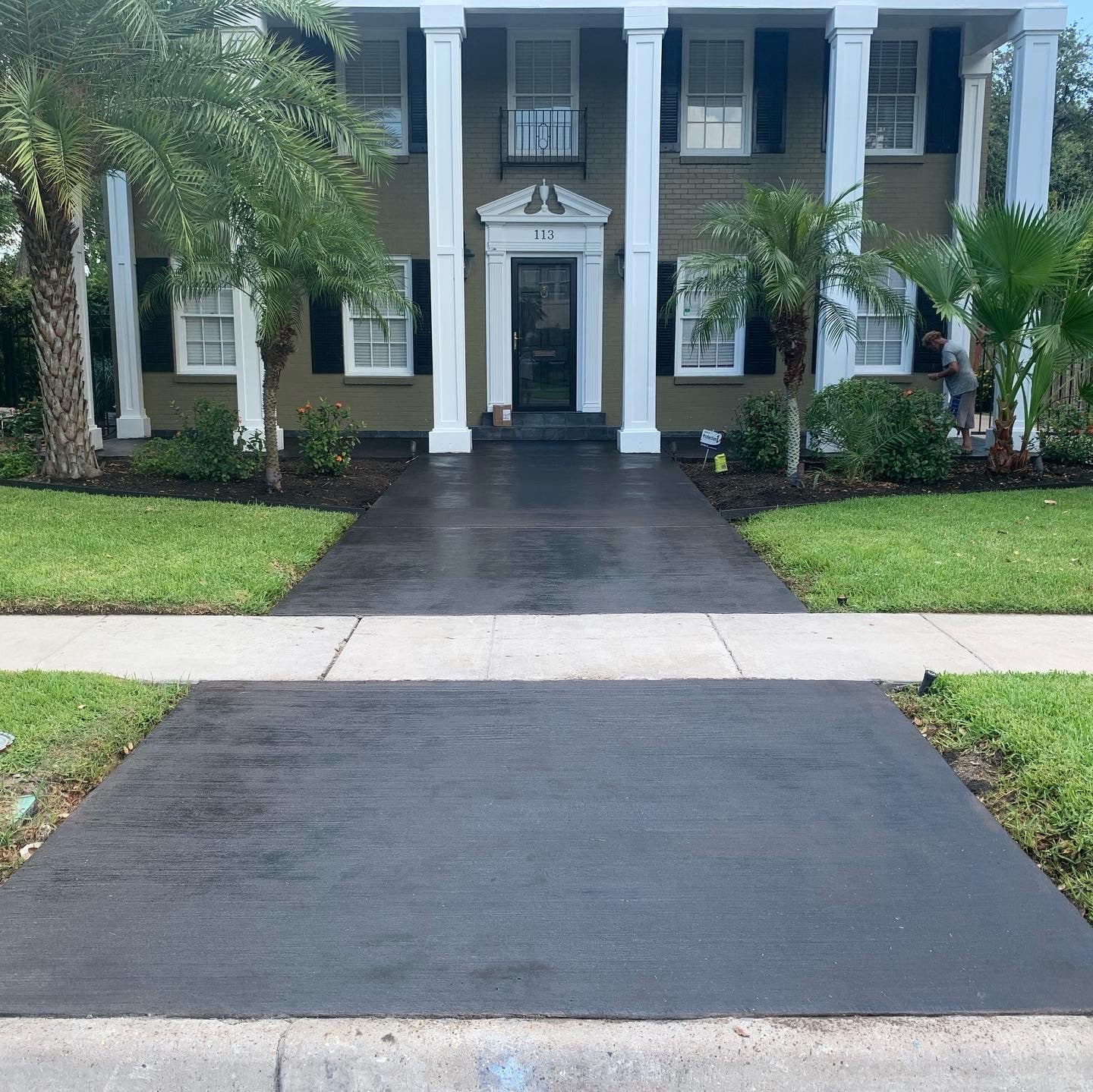 Charcoal acid-stained concrete driveway leading to a white colonial-style home