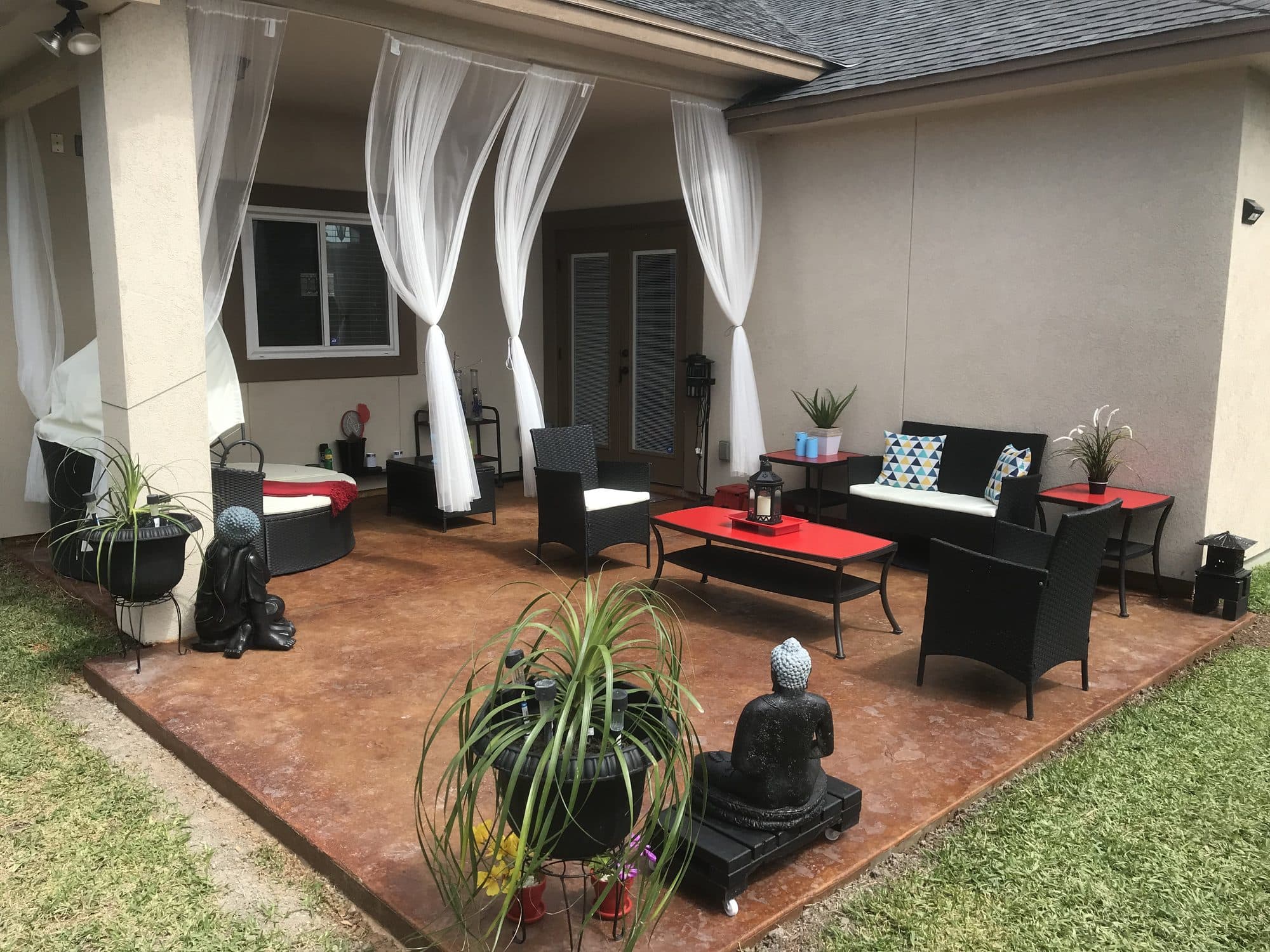 Covered patio with white curtains and wicker seating on acid-stained concrete