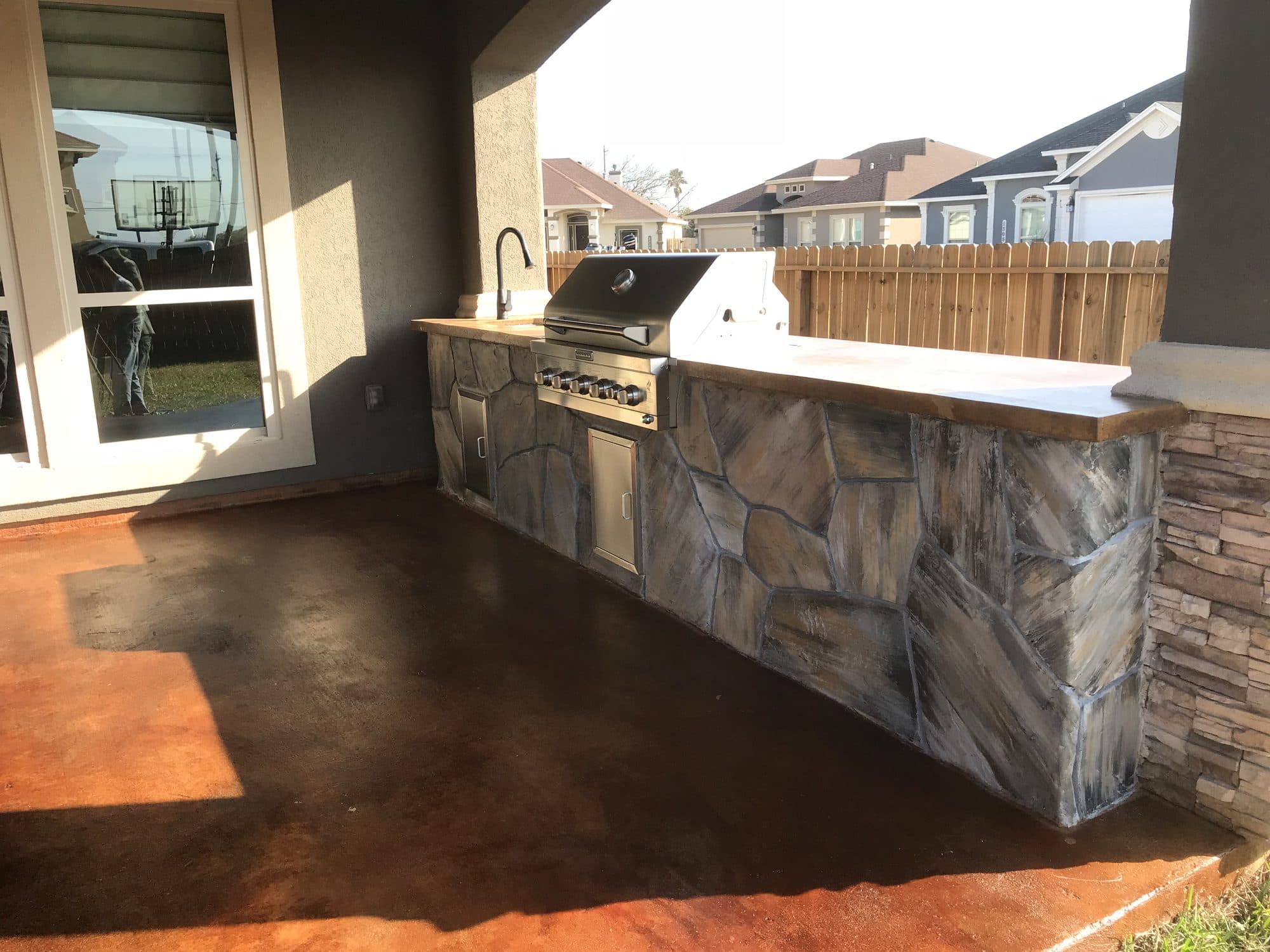 Stone-faced outdoor kitchen with a built-in grill on an acid-stained patio