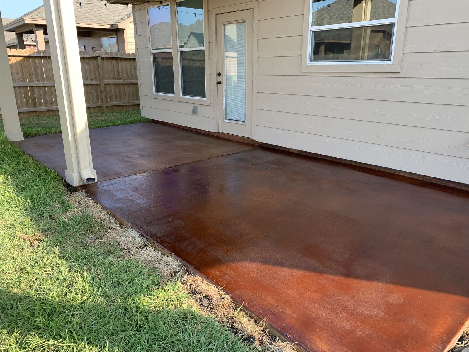 Red-brown acid-stained back patio along the side of a home