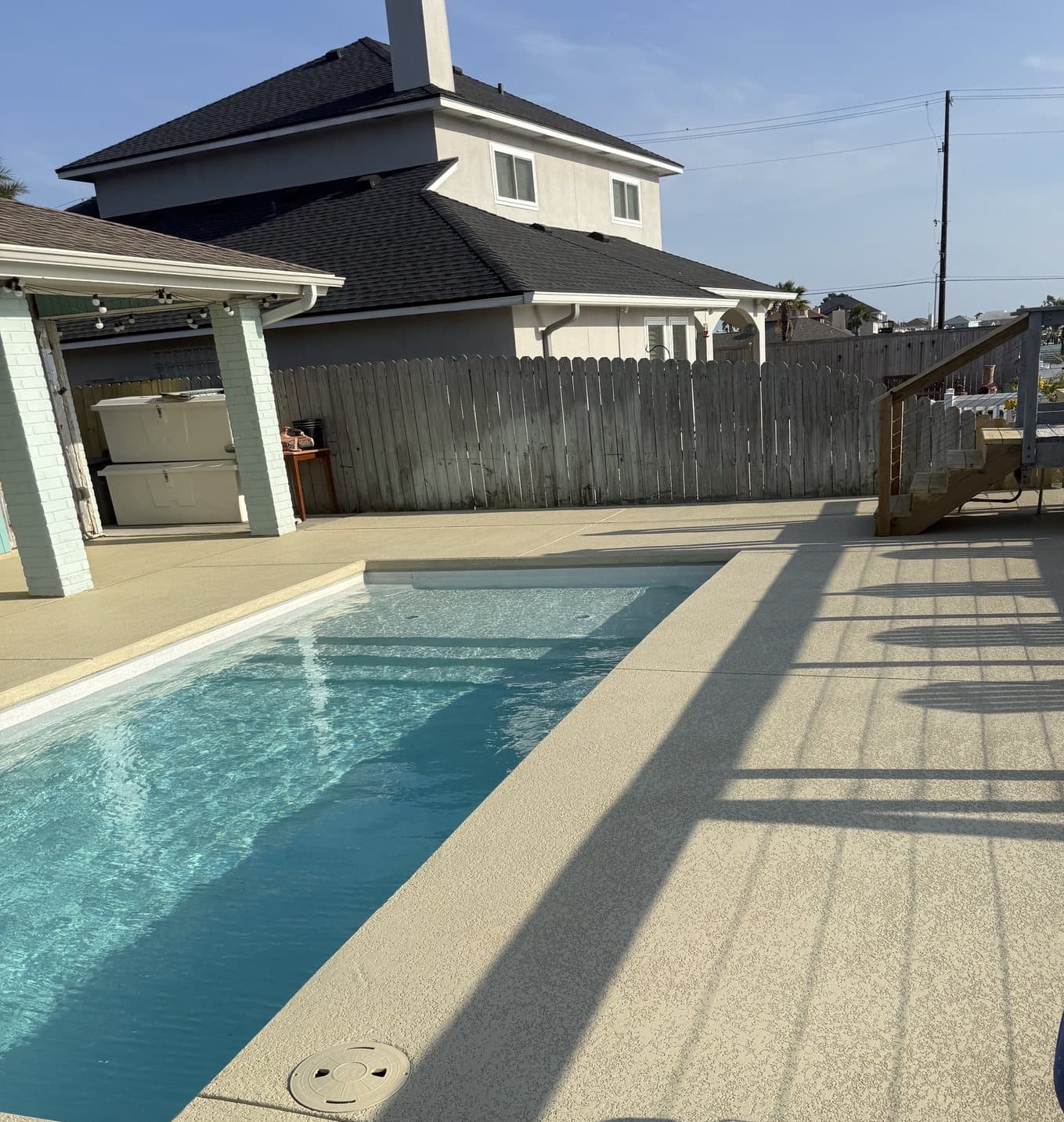 Tan knockdown cool deck around a rectangular pool, with a wooden deck and stairs at the far end