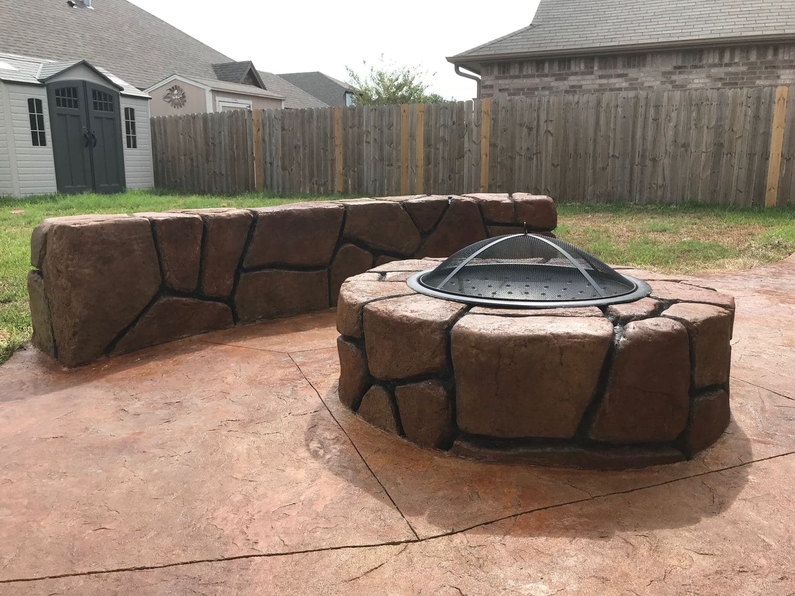 Stamped stone-look fire pit with a matching curved seat wall on a stained patio