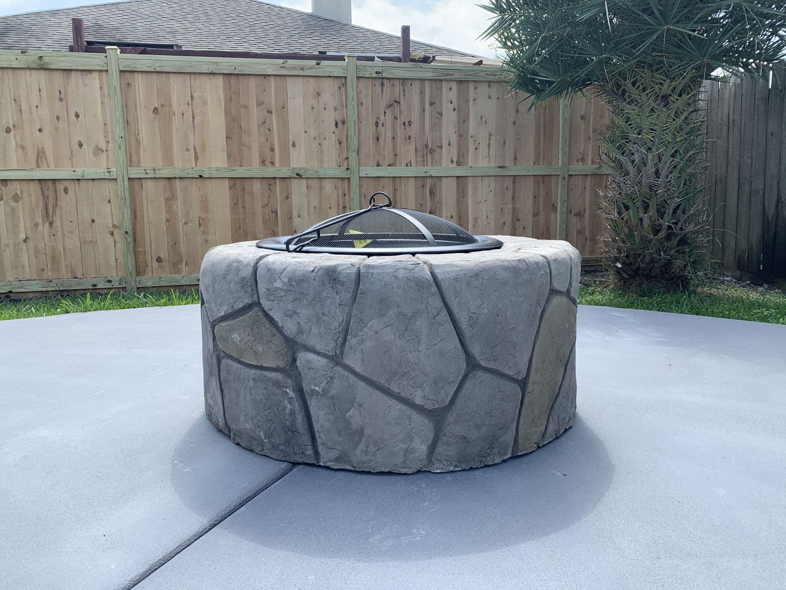 Stone-look fire pit on a new concrete slab by a cedar fence