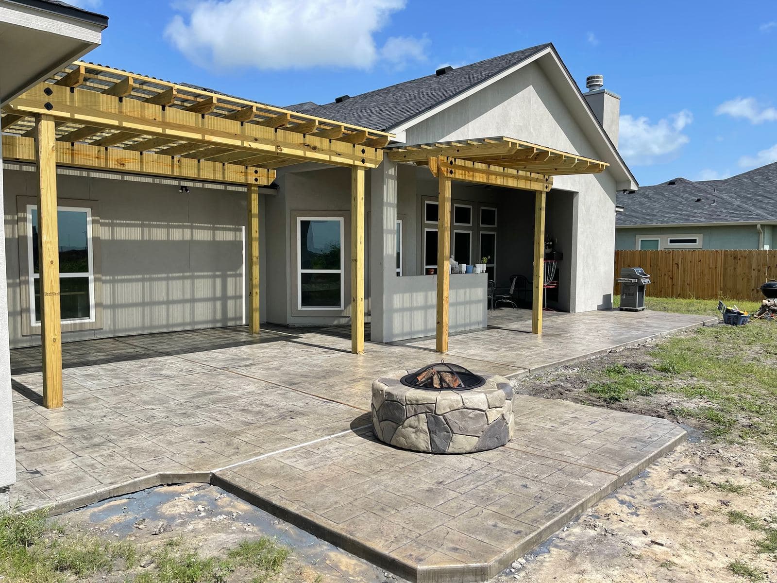 Stone-look fire pit on a stamped patio beside a new pergola