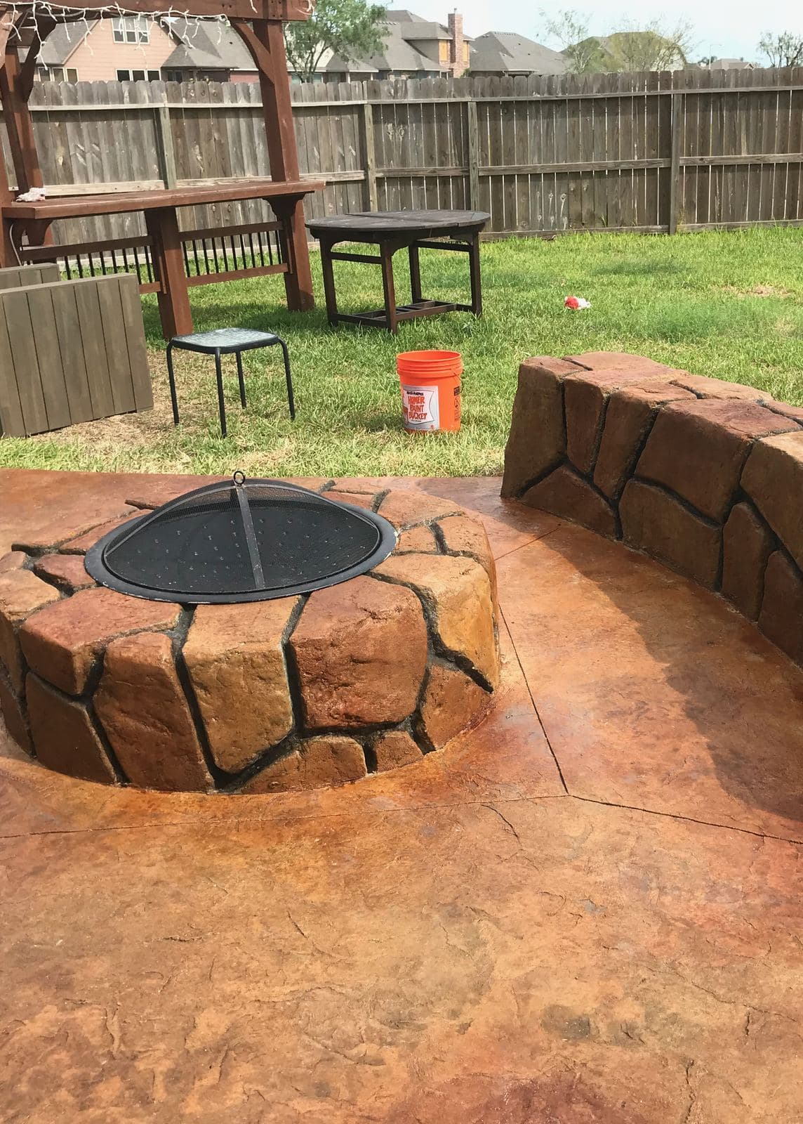 Stone-look fire pit and seat wall on a stained stamped patio in a fenced yard