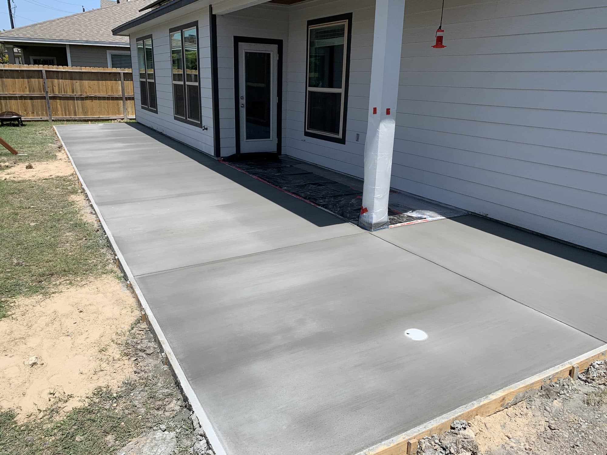 New broom-finished concrete patio beside a white home