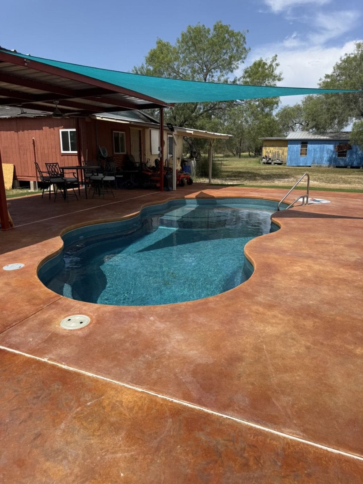 Acid-stained pool deck under shade sails around a freeform fiberglass pool