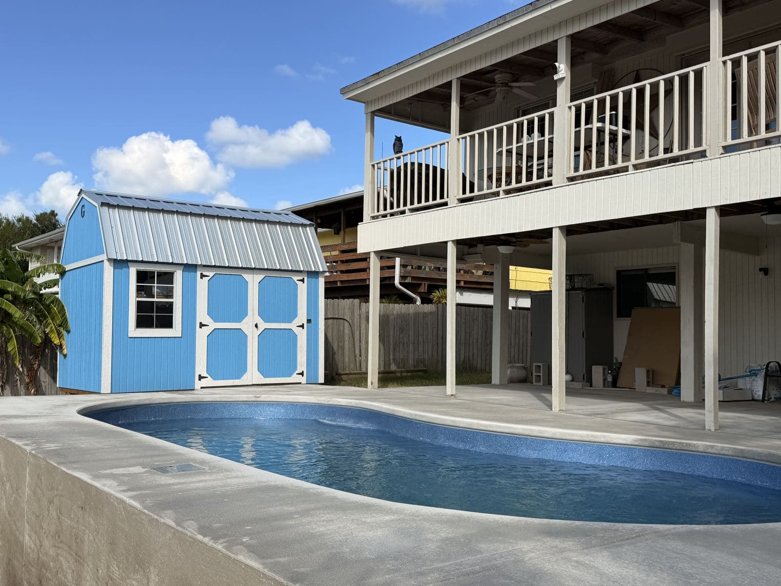 Fiberglass pool and deck between a blue shed and a raised coastal home