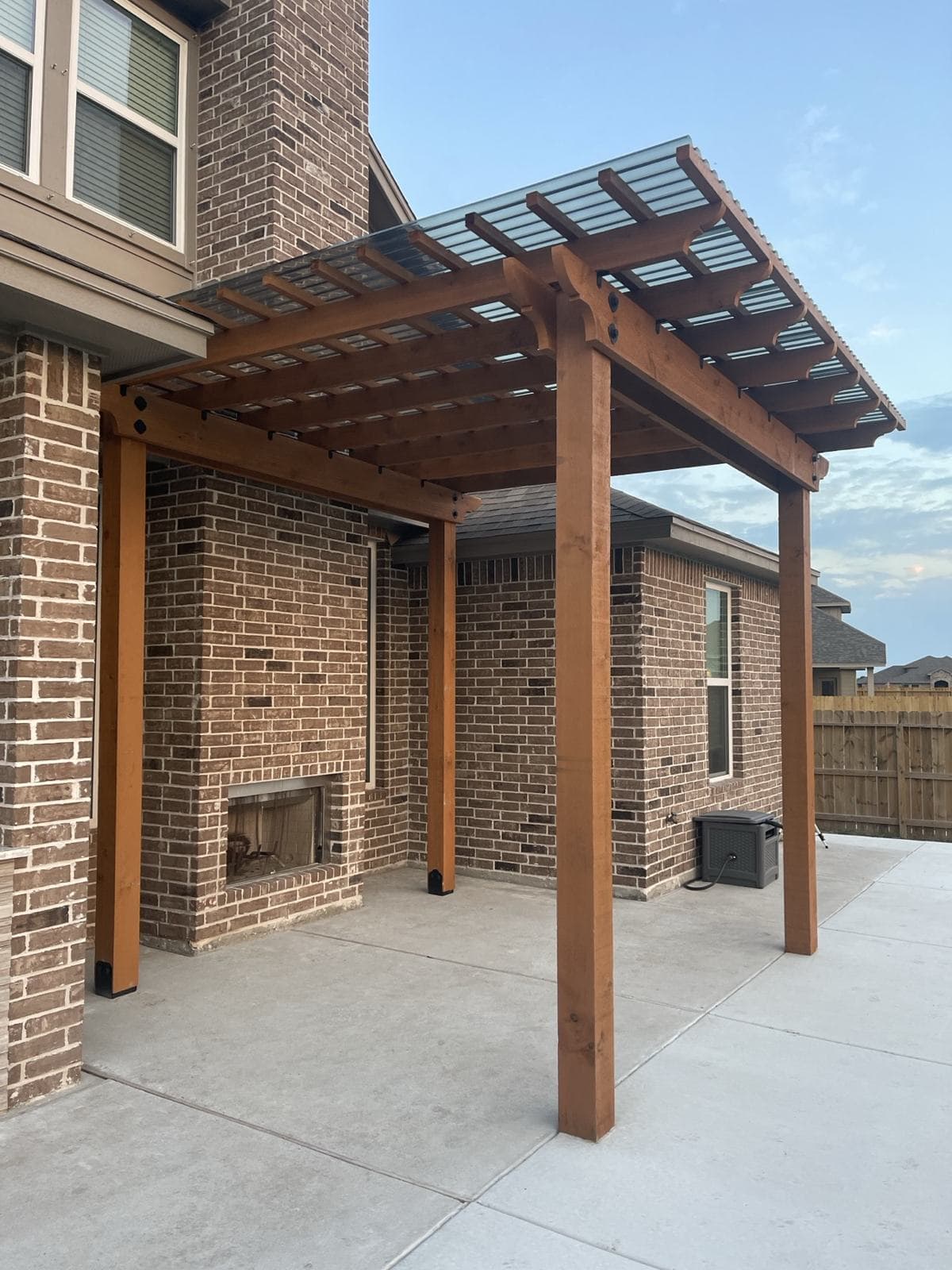 Cedar pergola attached to the back of a brick home over a stamped patio
