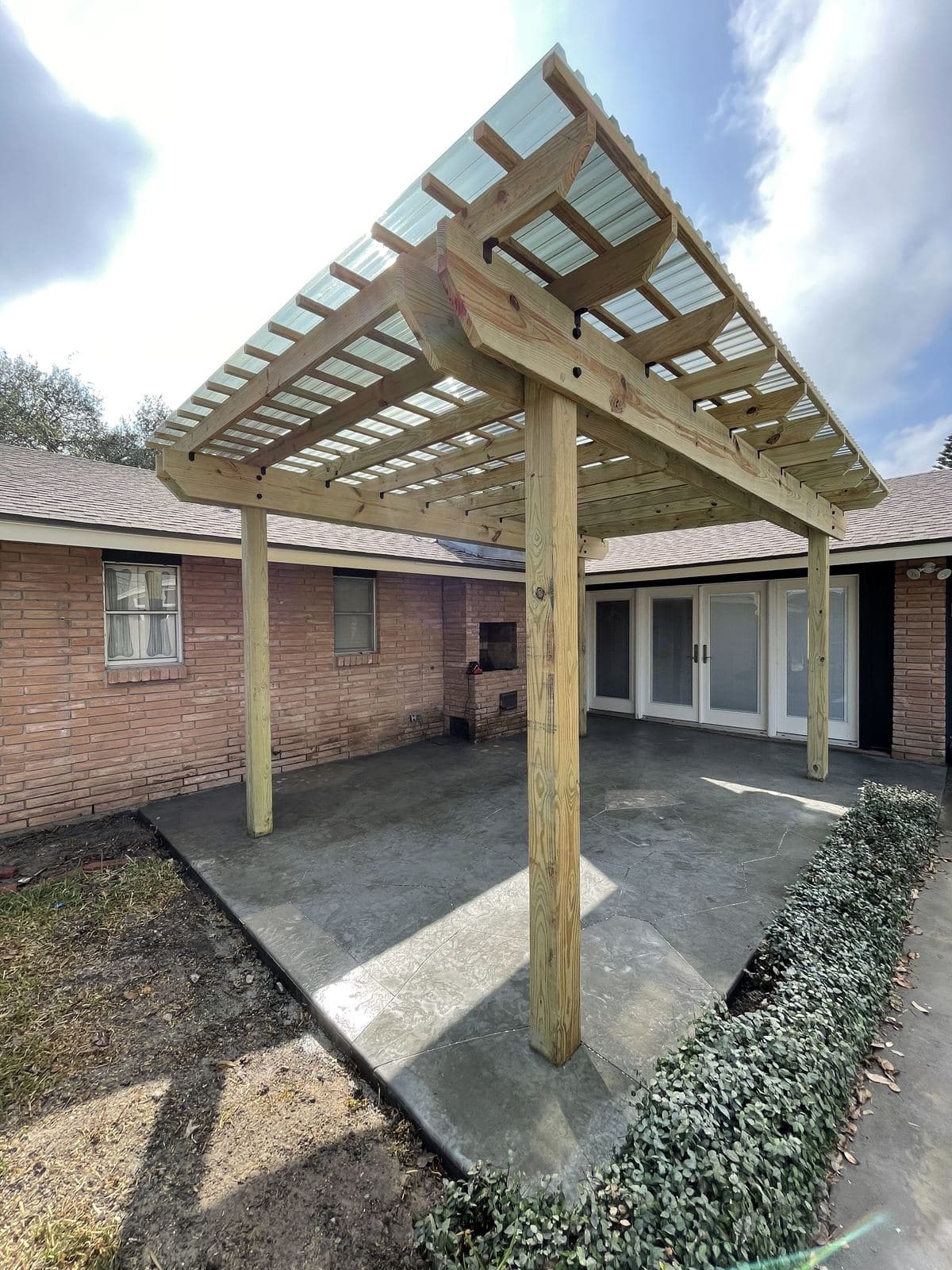 Freshly built cedar pergola over a new concrete patio beside a brick home