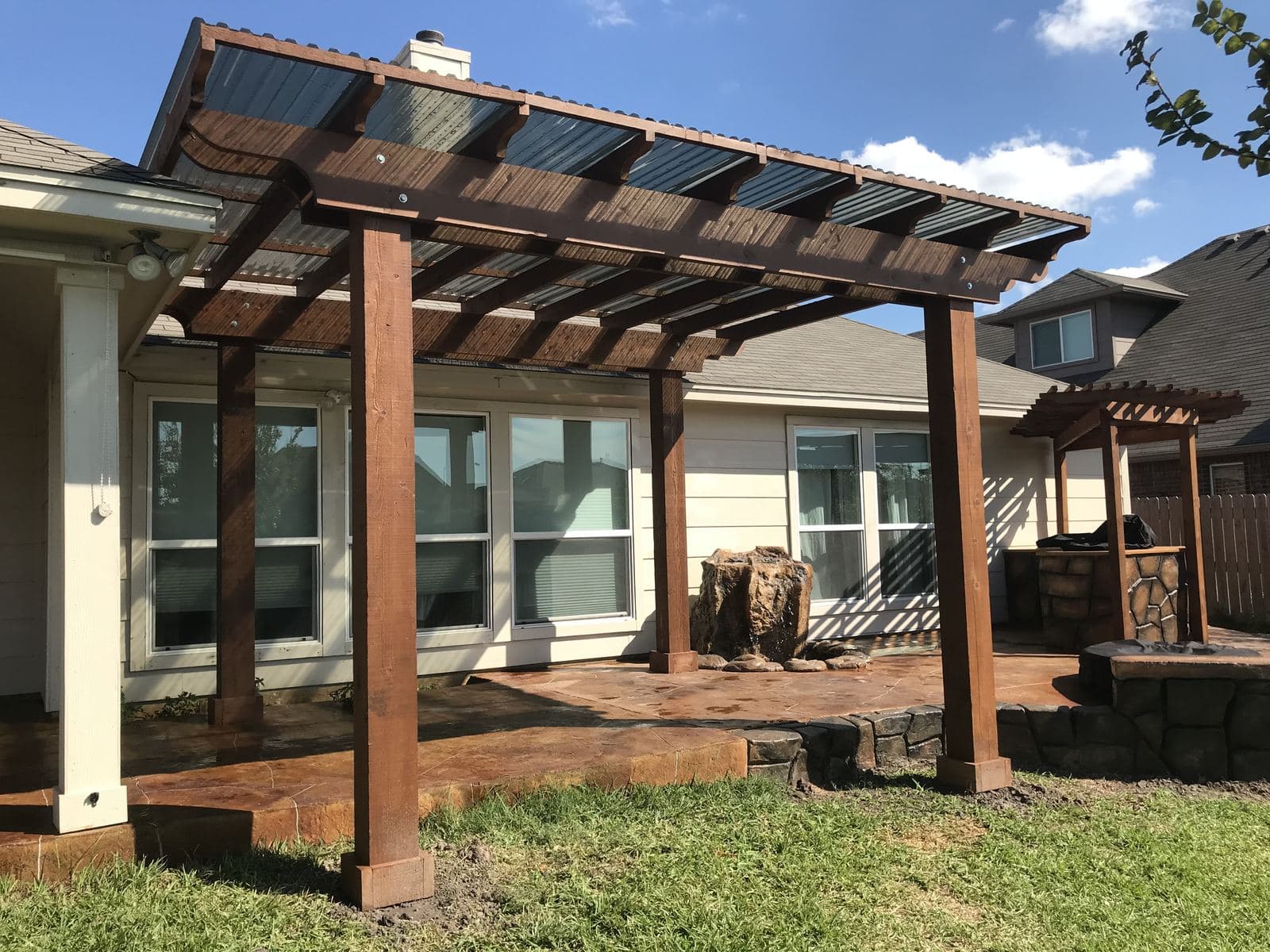 Cedar pergola over a stained patio across the back of a home