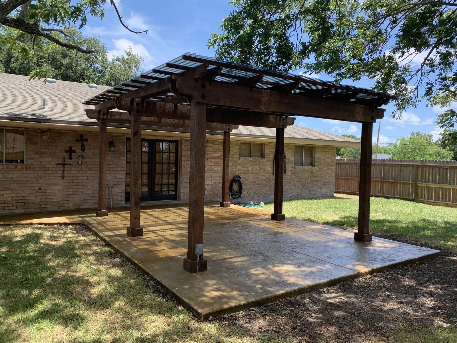 Dark-stained pergola over a new concrete patio behind a brick home