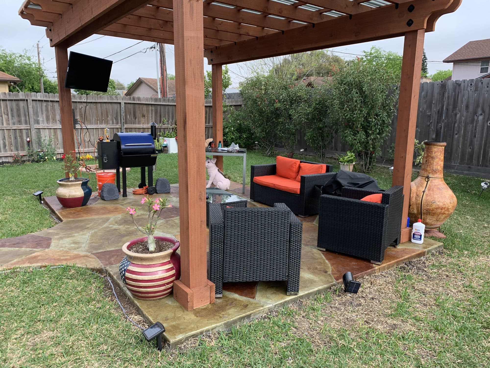 Cedar pergola over a flagstone-stained patio with seating, a TV and a grill