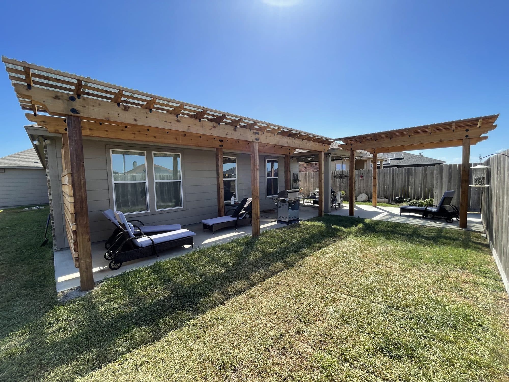Long cedar pergola running along the back of a home with loungers