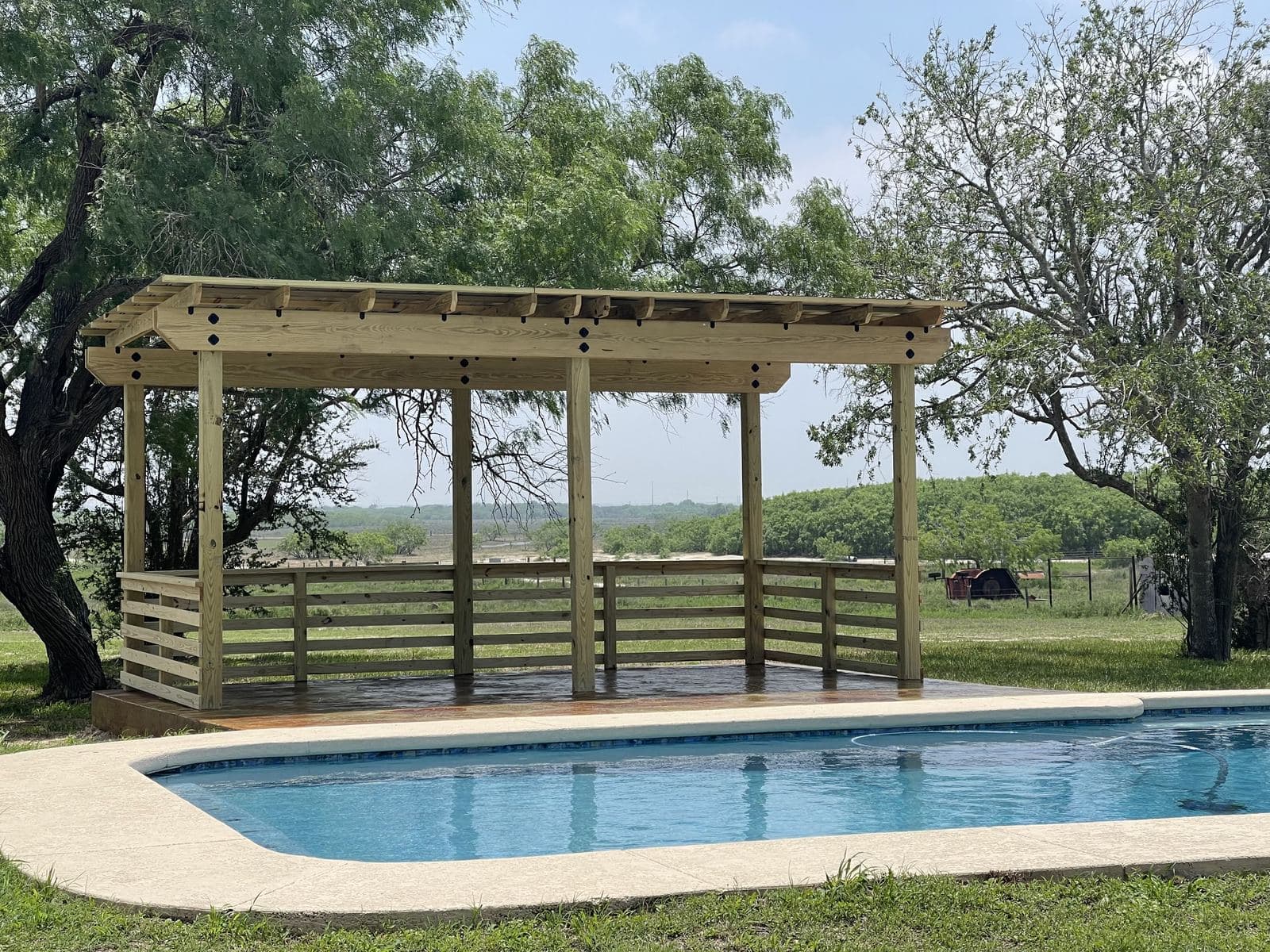 Pergola with a wood railing beside a pool in the country