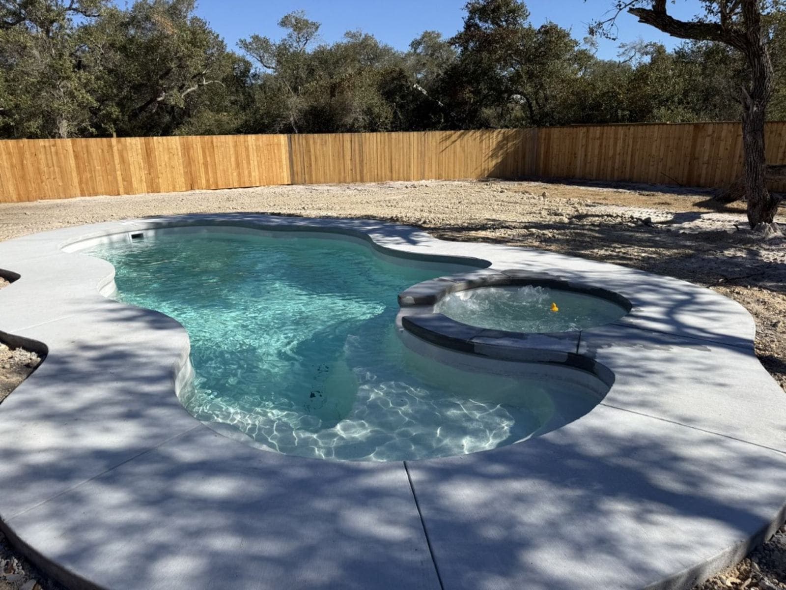 Finished fiberglass pool and concrete deck in a fenced back yard