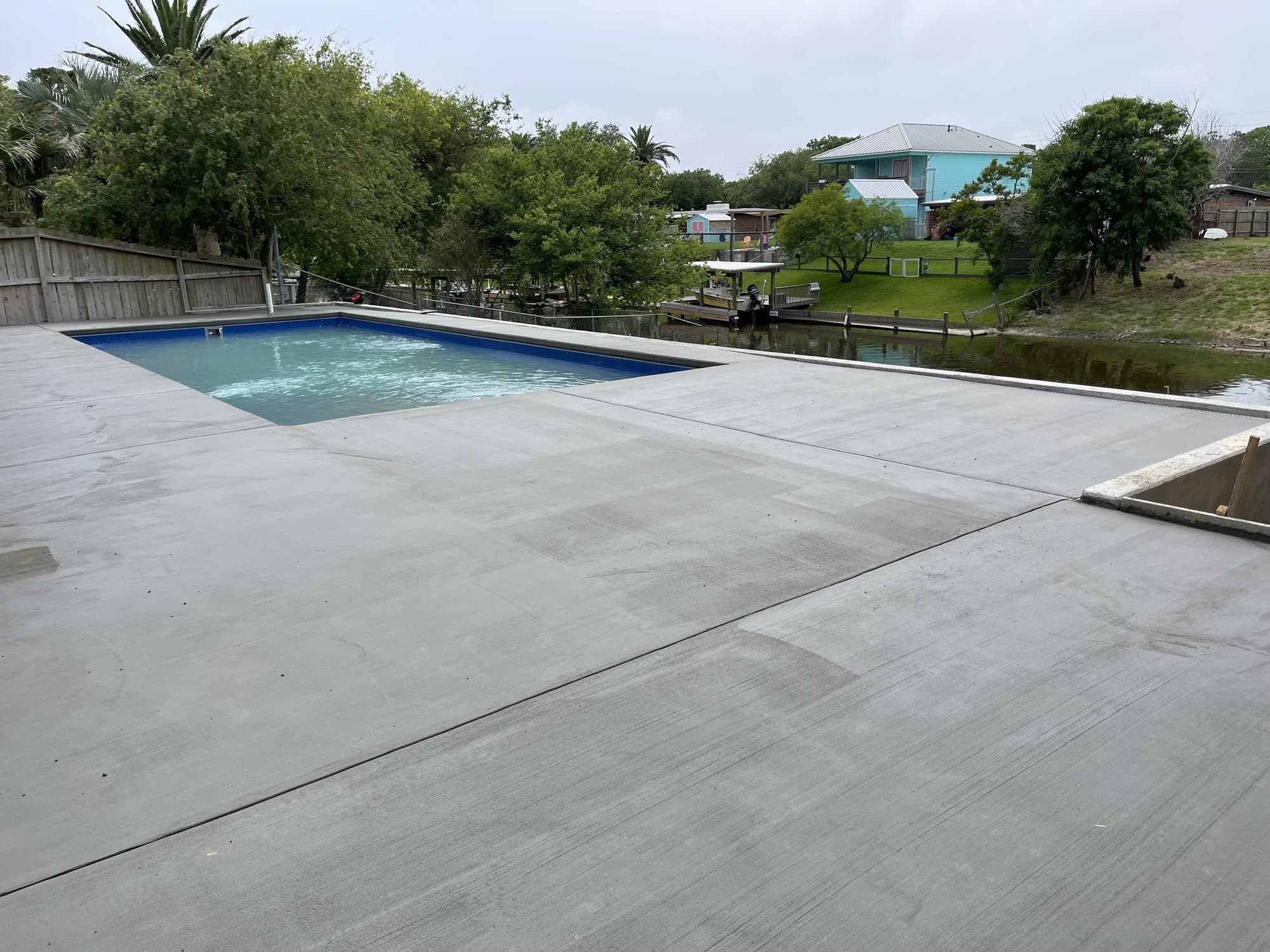 Broom-finished pool deck beside a rectangular pool on a waterfront lot
