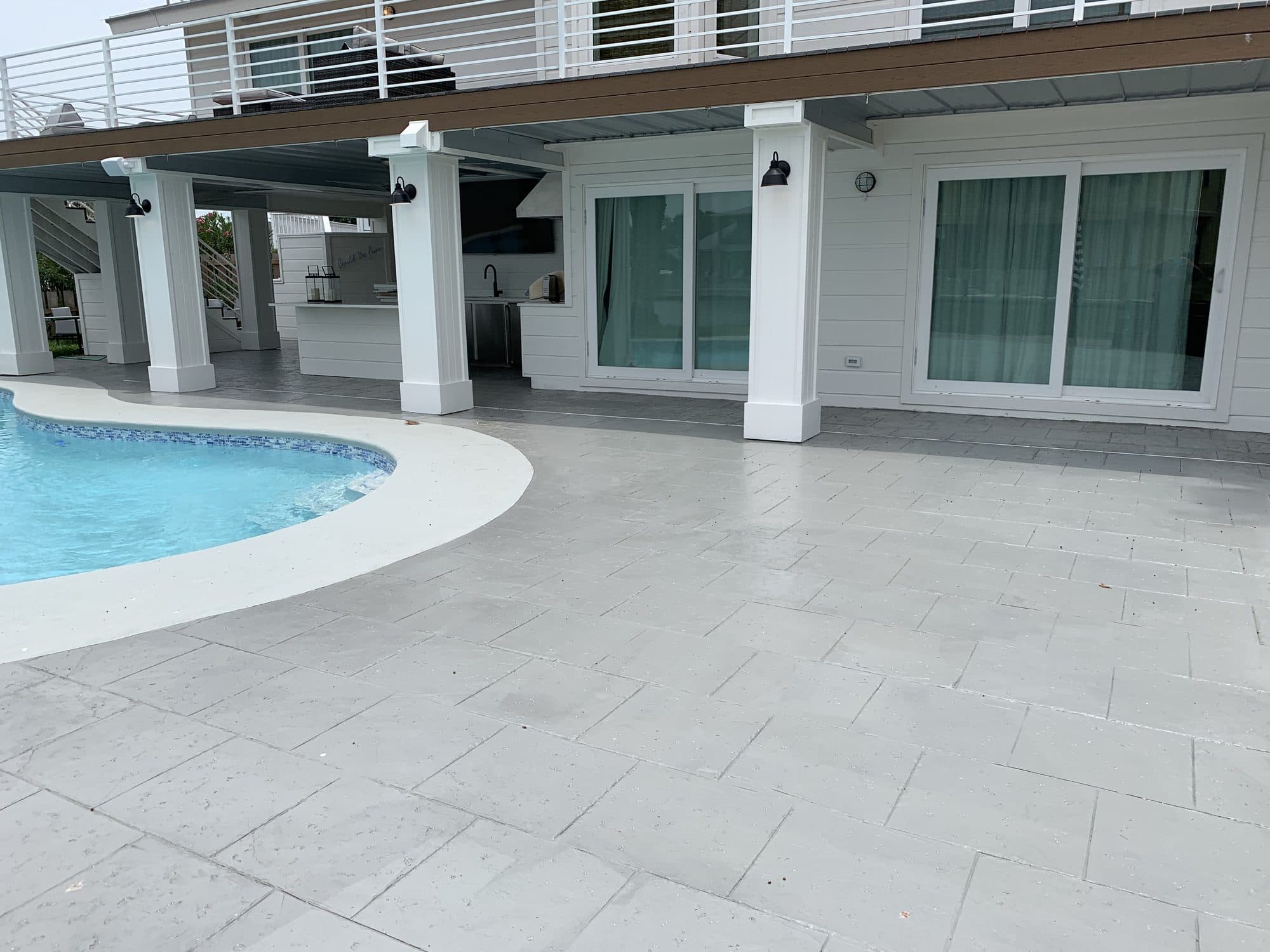 Large gray stamped pool deck wrapping a freeform pool beside a covered patio