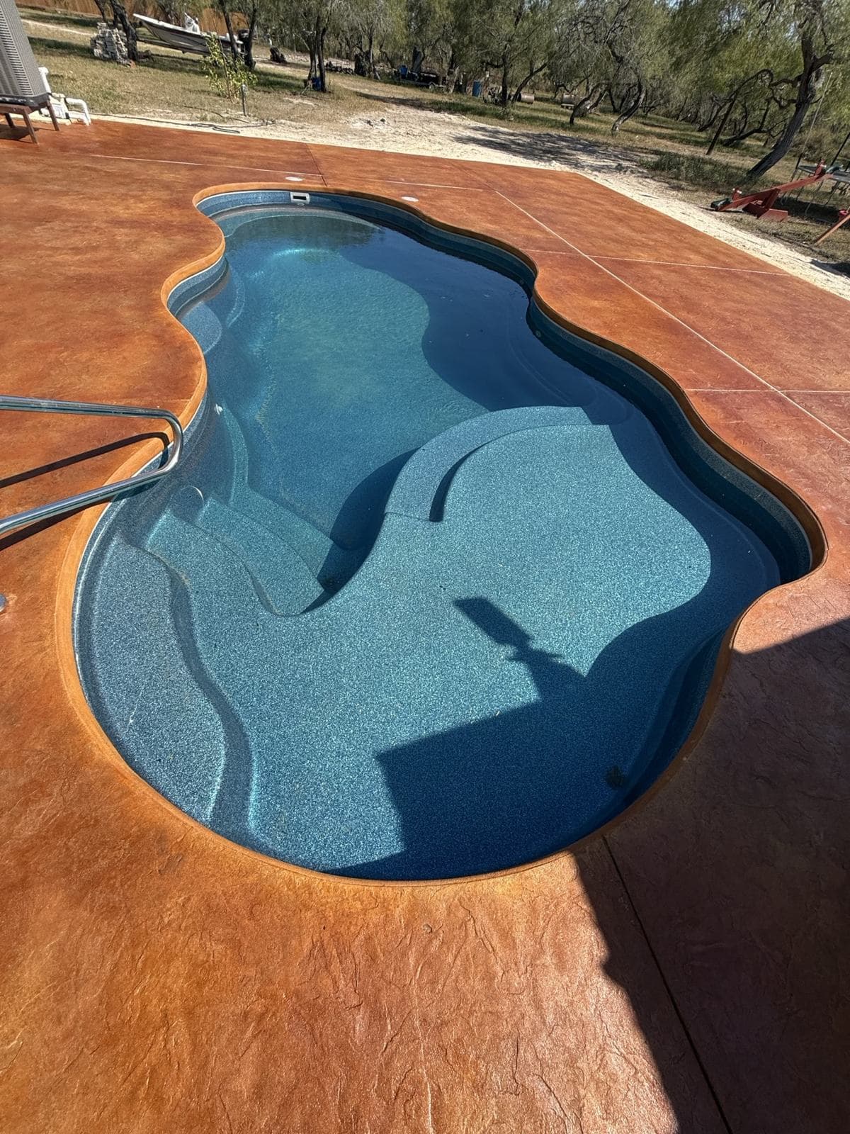 Freeform pool with a terracotta-stained concrete deck