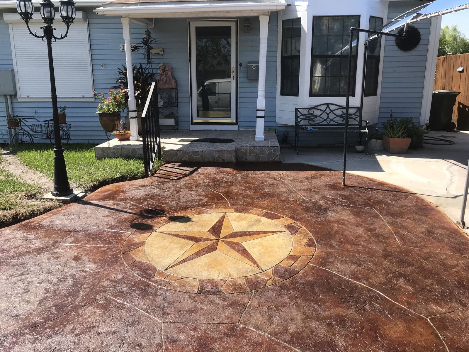 Stained stamped front courtyard with a Texas star inlay in front of a blue home