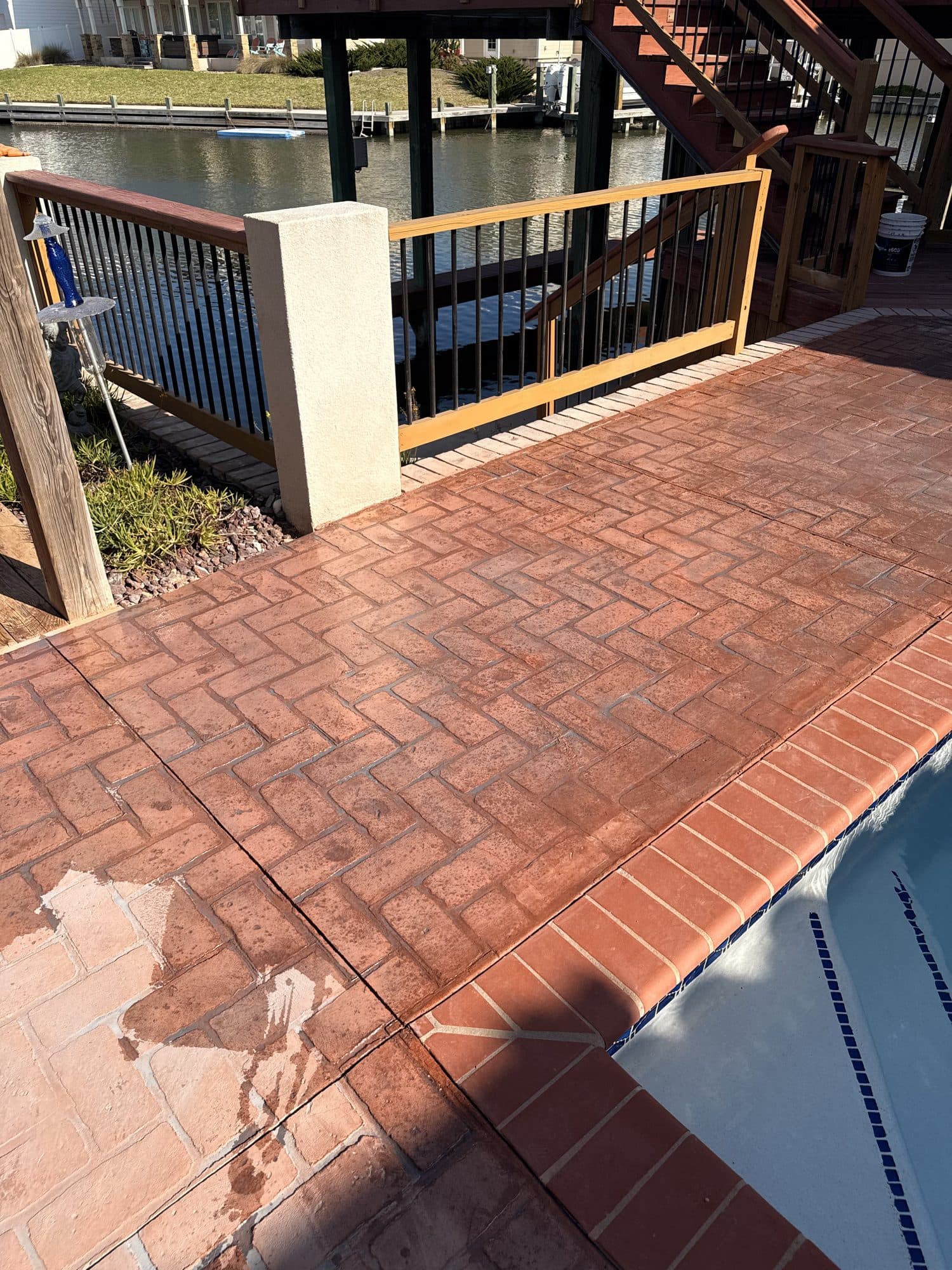 Red herringbone brick-pattern stamped concrete deck beside a pool on the waterfront