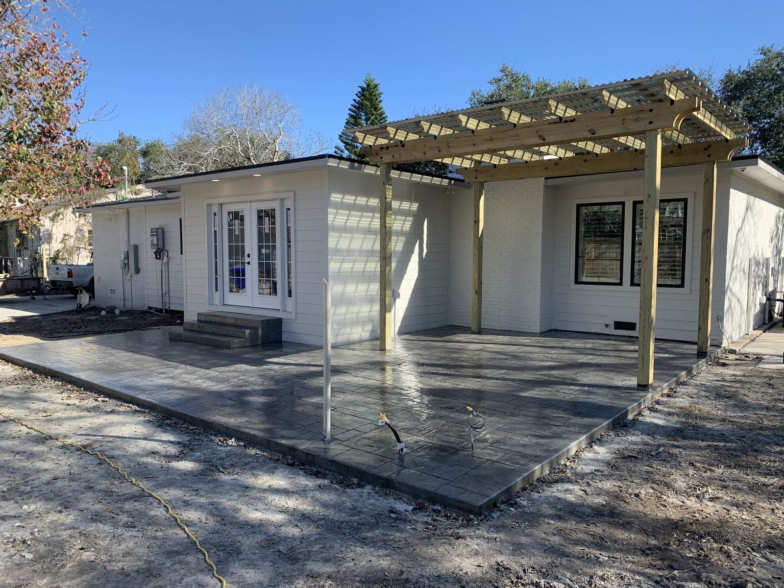 New concrete patio with a cedar pergola across the back of a white home