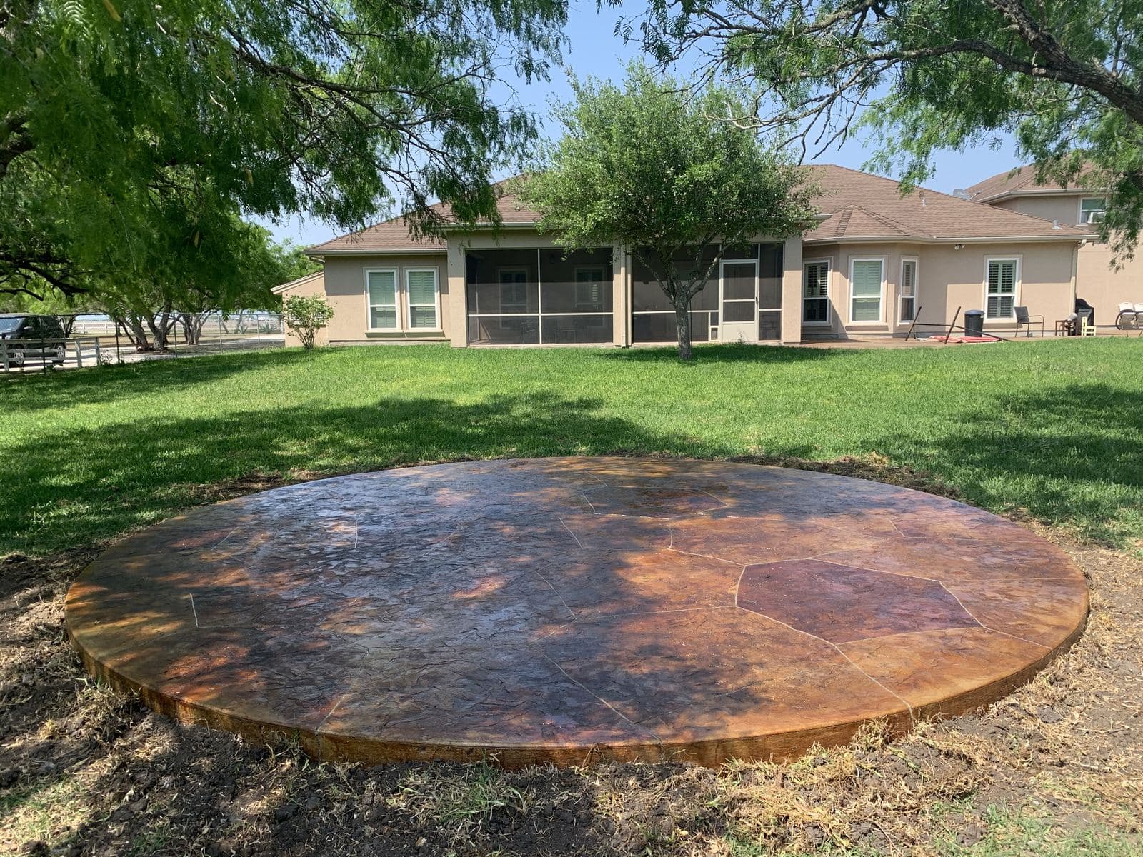 Round stained stamped concrete patio in a large back lawn